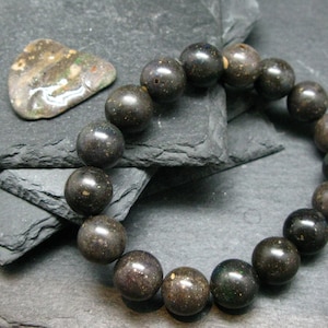 May include: A black opal beaded bracelet on a dark grey background. The beads are round and have a slight shimmer.