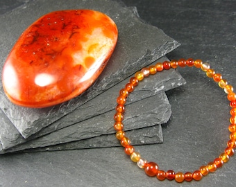 May include: A carnelian bracelet with orange and red beads, and a large carnelian stone with orange and red hues.