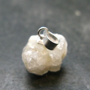 May include: A raw, translucent white crystal pendant featuring an irregular, multifaceted shape. The stone is securely attached to a polished silver-toned metal bail, designed for threading onto a chain or cord for use as a necklace accessory.