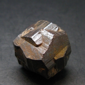 May include: A faceted, cubic pyrite crystal with a metallic lustre. The mineral specimen displays a dark, brownish-gold colour with sharp, well-defined edges. The surface has a slightly rough texture.