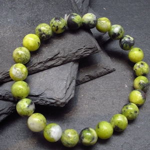 May include: A green and black gemstone bracelet with round beads. The bracelet is made of natural stones and is strung on a clear elastic cord.