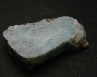 May include: A light green and white rough-cut stone with a smooth, polished surface.