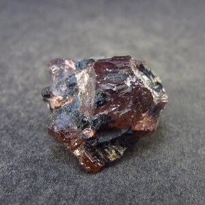 May include: A close-up of a dark red and black crystal with a rough, irregular surface. The crystal has a sharp, angular shape and appears to be translucent.