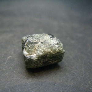 May include: A dark green, faceted, rough-cut gemstone with a square shape.