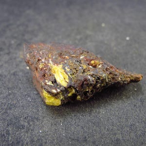 May include: A rough, dark brown and gray rock with a patch of bright yellow crystals. The rock has a natural, unpolished surface.
