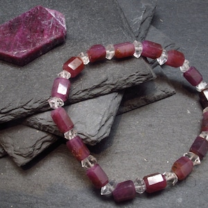 May include: A bracelet made with faceted ruby and clear quartz beads. The bracelet is on a dark grey background.