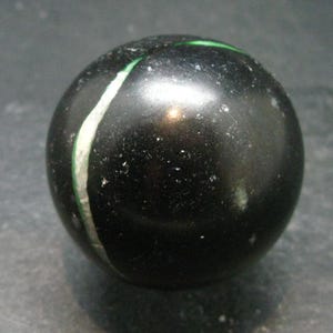 May include: A black glass marble with a green and white stripe.