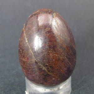 May include: A smooth, polished, red ruby egg with a dark red and brown striated pattern.