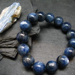 Könnte beinhalten: Ein Armband aus großen, polierten, tiefblauen Perlen mit marmoriertem Aussehen. Ein rauer, hellblauer und beigefarbener Stein liegt in der Nähe. Die Perlen haben einen Durchmesser von etwa 3,2 cm. Das Armband ist ein Schmuckstück.