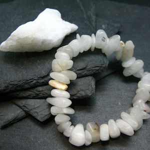 May include: A white gemstone bracelet with gold accents. The bracelet is made of smooth, rounded stones and is strung on a clear elastic cord.