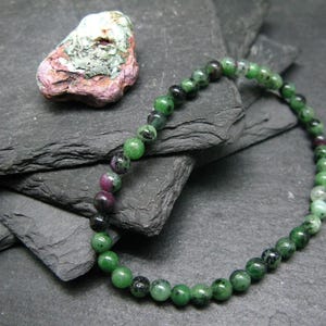 May include: A green and pink gemstone bracelet with round beads. The bracelet is made of natural stones and is approximately 7 inches in length.