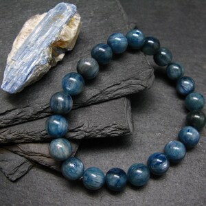 Könnte beinhalten: Ein blaues Kyanit-Perlenarmband mit einem natürlichen Steinakzent. Das Armband hat runde, polierte Perlen in Blau- und Türkistönen. Der Kyanitstein ist hellblau und hat eine raue Textur.