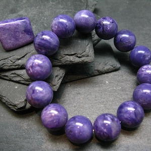 May include: A purple gemstone bracelet with round beads and a matching square pendant.