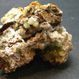 May include: A cluster of green and white crystals embedded in a brown rock matrix. The crystals are translucent and have a glassy lustre.