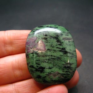 Puede incluir: Una piedra preciosa lisa, verde y negra con inclusiones rosadas y blancas. La piedra está pulida y tiene una forma natural y orgánica.