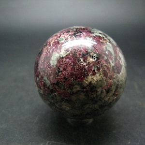 May include: A smooth, round sphere of red and green uvarovite, a rare gemstone, polished to a high shine.