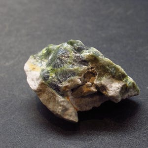 Pode incluir: Um close-up de uma rocha verde e branca com textura áspera. A rocha tem um aglomerado de cristais verdes em um lado.