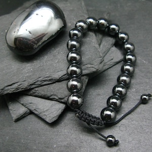Peut inclure: Un bracelet en perles d'hématite noire avec une fermeture en cordon noir. Le bracelet est présenté sur une surface en ardoise noire avec une grande pierre d'hématite.