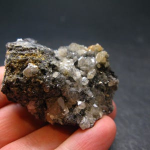 May include: A close-up of a mineral specimen featuring a dark, textured matrix with clusters of small, sparkling crystals. The crystals are primarily clear and translucent, with hints of yellow and brown. The overall appearance is rough and natural.