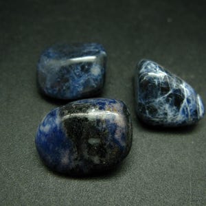May include: Three smooth, polished stones of blue sodalite. The stones are various shades of blue with white veining and black inclusions.