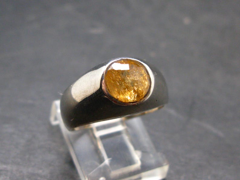 Puede incluir: Un anillo de plata con una gema grande y redonda de color &aacute;mbar. El anillo tiene una banda ancha y un acabado pulido, que muestra los tonos c&aacute;lidos de la gema. La gema est&aacute; engastada en un engaste de bisel.