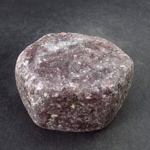 May include: A large, rough, purple gemstone with a hexagonal shape. The gemstone has a rough, textured surface and is a deep purple color.