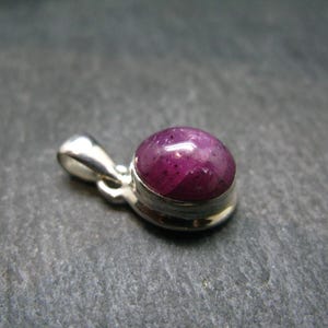 May include: A silver pendant featuring a round, cabochon-cut, pink ruby gemstone.