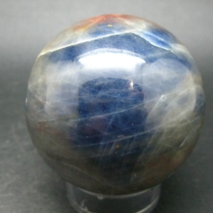 Puede incluir: Una esfera de piedra preciosa azul, gris y blanca. La esfera está pulida y tiene una superficie lisa y brillante.