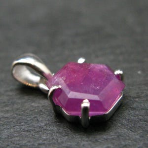 May include: A pendant featuring a faceted, hexagonal-cut pink gemstone set in a silver-toned metal prong setting. The stone has a translucent appearance with visible internal inclusions and is attached to a polished silver-toned metal bail.