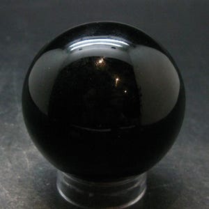 May include: A smooth, polished, spherical object in a deep, solid black colour. The surface of the sphere is highly reflective, showing bright white light highlights from the surrounding environment, creating a glossy and uniform appearance.