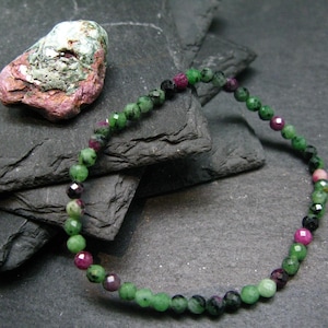May include: A green and pink gemstone bracelet with round beads. The bracelet is made of green, pink, and black beads.
