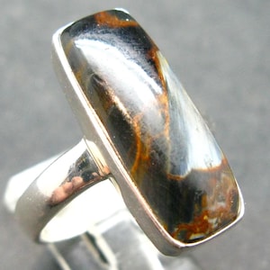 May include: A silver ring featuring a rectangular, iridescent blue and brown gemstone. The gemstone has a distinctive, swirling pattern.