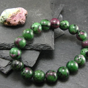 May include: A green and pink gemstone bracelet with round beads. The bracelet is made of natural stones and is approximately 8 inches in length.