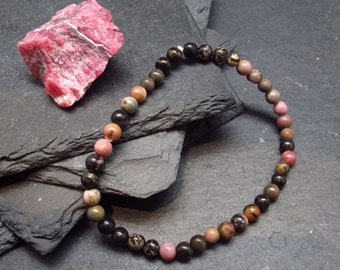 May include: A pink, brown, and black beaded bracelet made of natural stones. The bracelet is on a dark gray background.