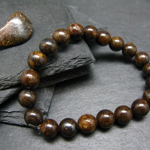 Puede incluir: Un brazalete de piedras preciosas marrón y dorado con cuentas redondas. El brazalete está hecho de piedras naturales y tiene un cierre plateado.