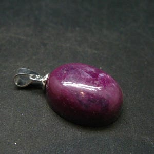 May include: A purple gemstone pendant with a silver bail. The gemstone is oval shaped and has a smooth, polished surface.