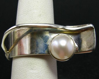 May include: A silver ring with a wavy design and a large white pearl.
