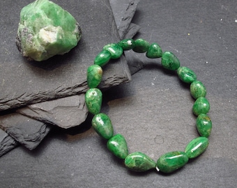 May include: A green gemstone bracelet made of smooth, teardrop-shaped beads. The bracelet is laid out on a dark gray slate surface.