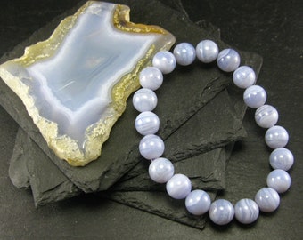 May include: A blue agate gemstone bracelet with round beads. The bracelet is made of natural stones and has a light blue color with white stripes.