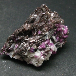 May include: A cluster of dark brown and black crystals with small, bright pink crystals embedded throughout. The crystals are arranged in a rough, natural formation.