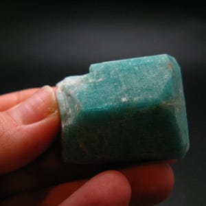 Puede incluir: Un cristal de amazonita verde, facetado y en bruto. El cristal es una piedra preciosa natural y tiene un aspecto ligeramente nublado.