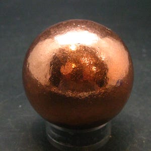 Puede incluir: Una esfera de color cobre con una superficie brillante y texturizada.