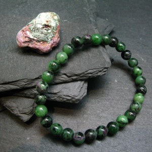 Puede incluir: Un brazalete de piedras preciosas verdes y negras con cuentas redondas. El brazalete está hecho de piedras naturales y tiene una longitud aproximada de 18 cm.