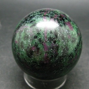 Könnte beinhalten: Eine grüne und violette Edelsteinkugel, auch bekannt als Zultanit, mit einer glatten, polierten Oberfläche.