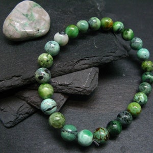 May include: A green and brown gemstone bracelet with round beads. The bracelet is on a black slate background.