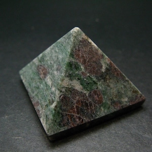May include: A pyramid-shaped stone object featuring a mottled surface with deep forest green and dark reddish-brown mineral inclusions. The stone has a polished finish with visible natural crystalline textures throughout its four triangular faces.
