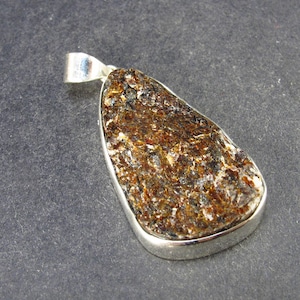 May include: A silver pendant with a brown, rough, and textured stone. The stone is set in a silver bezel and has a teardrop shape.