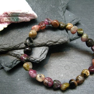 May include: A bracelet made of multi-colored, tumbled, watermelon tourmaline beads. The beads are a mix of pink, green, black, and brown.
