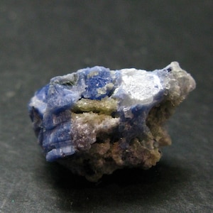 May include: A raw mineral specimen featuring deep blue crystalline structures interspersed with translucent white and pale yellow mineral deposits. The rough, jagged rock formation displays a variety of textures and natural geometric facets.