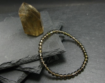 May include: A brown gemstone bracelet with small, round beads. The bracelet is lying on a stack of black slate tiles. A large, clear, brown gemstone is also visible in the image.